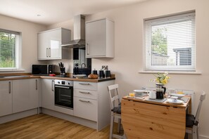 Eine moderne Küche mit weißen Schränken, einem Einbauofen und einem Essbereich mit Holztisch und -stühlen.