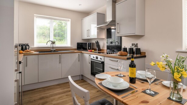 A modern kitchen with white cabinets, a built-in oven, and a dining area with a table set for two. - Apartment 3 (Holyhead)