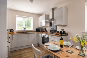 A modern kitchen with white cabinets, a built-in oven, and a dining area with a table set for two. - Apartment 3 (Holyhead)