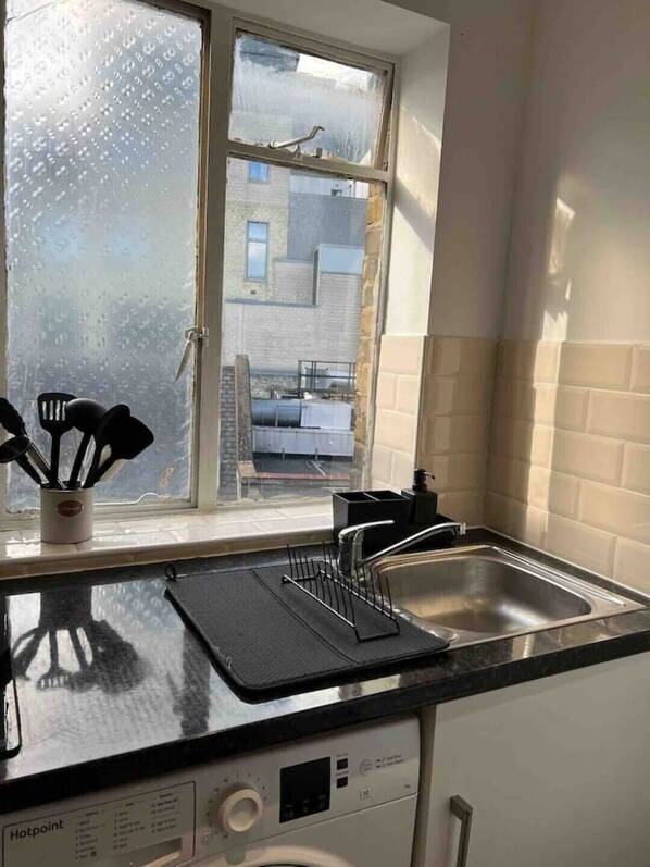 Compact kitchen with sink, washing machine, and window offering a view of the outside.