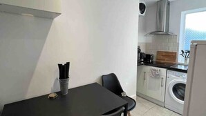 A compact kitchen with a dining table, chairs, a washing machine, and a stove.