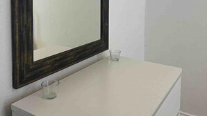 A bathroom with a white vanity, a dark wooden-framed mirror, and a small glass on the counter.