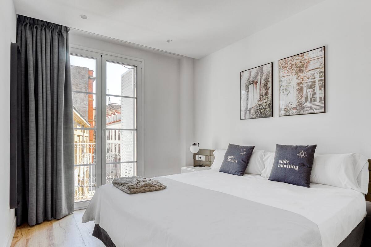 A bedroom with a large bed, a nightstand, a window with curtains, and two wall-mounted pictures.