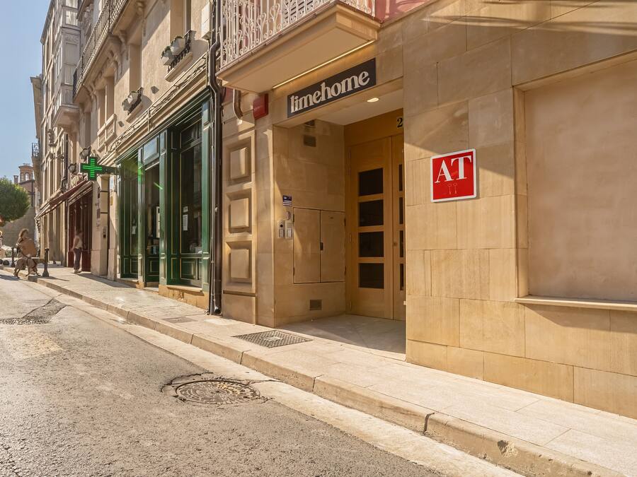 Un edificio con un letrero que dice 'timehome', una puerta marcada 'AT' y un toldo verde.