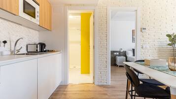 A modern kitchen with white cabinets, a microwave, and a toaster. There is a wooden dining table with chairs and a yellow accent wall.