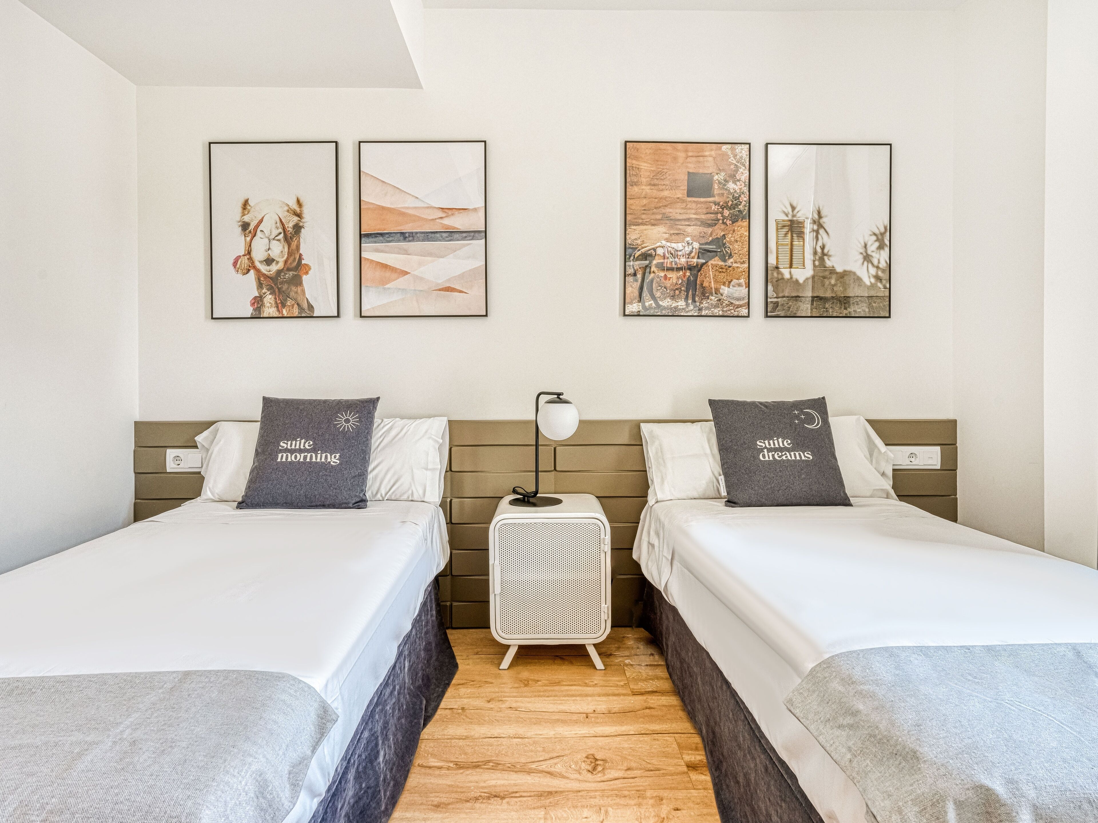 Habitación de hotel con dos camas, una mesita de noche y tres cuadros enmarcados en la pared.