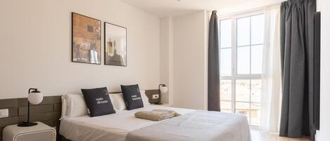 A neatly arranged bedroom with a bed, two pillows, a bedside lamp, a small heater, and a window with curtains.
