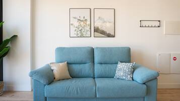 A light blue sofa with two cushions, a plant, and two framed pictures on the wall.