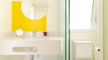 A bathroom with a white sink, a mirror, a glass shower enclosure, and a toilet.
