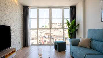 Una sala de estar moderna con un gran ventanal, un televisor de pantalla plana, un sofá azul y una mesa de centro de madera.