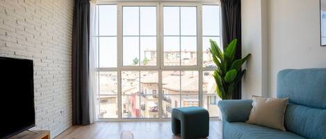 Una sala de estar moderna con un gran ventanal, un televisor de pantalla plana, un sofá azul y una mesa de centro de madera.