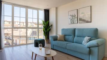 Una sala de estar moderna con un sofá azul, una mesa de centro, una planta en maceta y grandes ventanales con vistas a la ciudad.