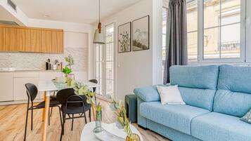 Una sala de estar moderna con un sofá azul, una mesa de comedor con sillas y una zona de cocina con armarios de madera.
