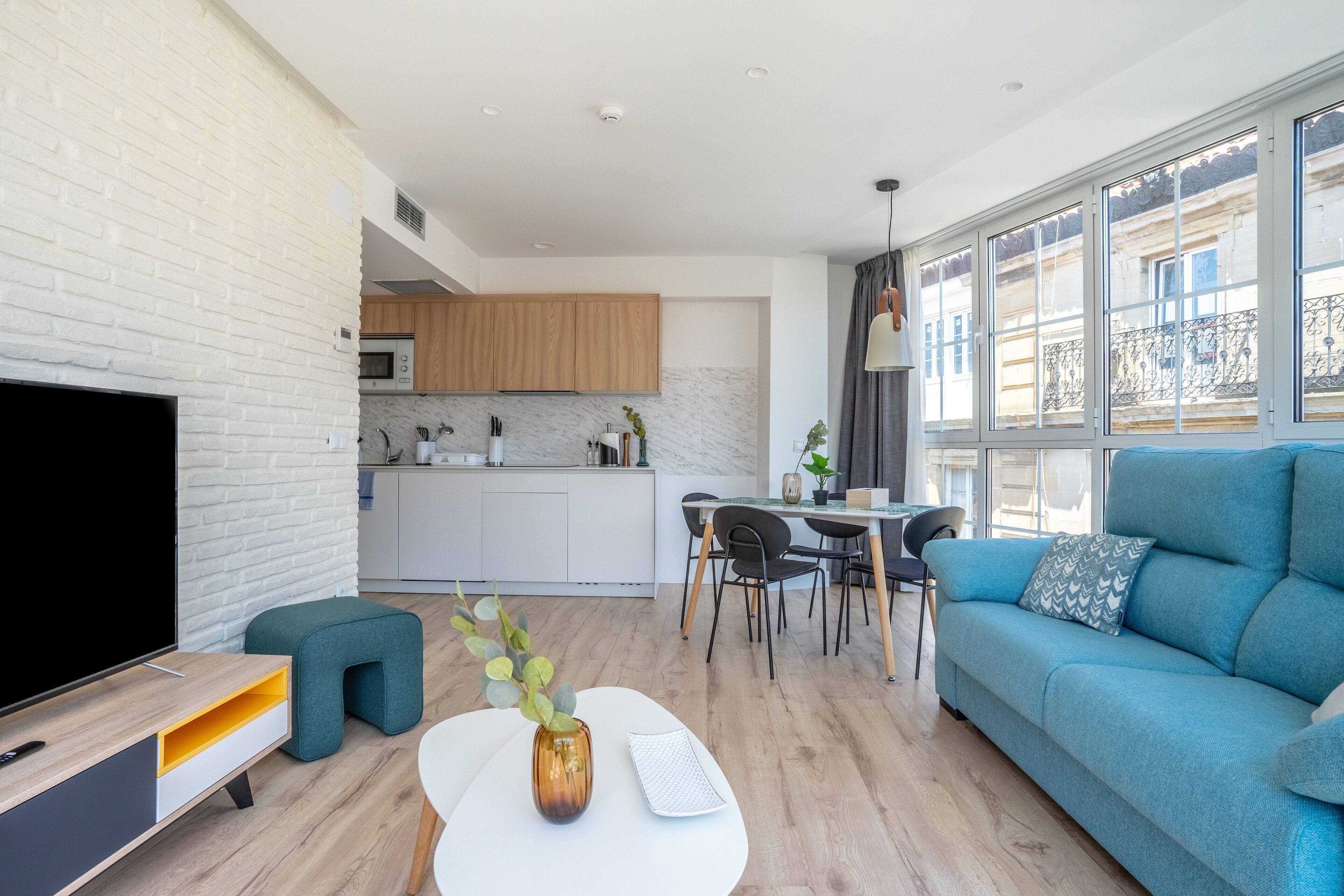 A modern living room with a flat-screen TV, a sofa, a coffee table, and a dining area with chairs and a table.