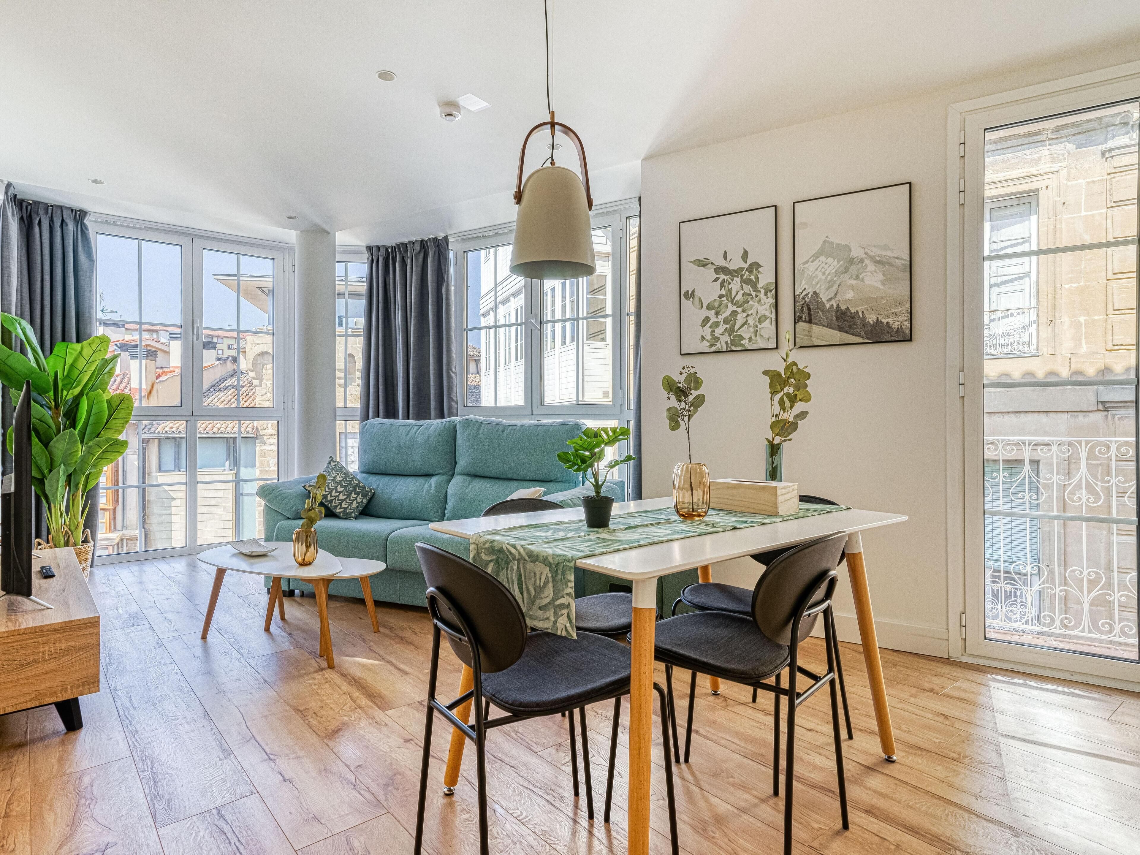 Una sala de estar moderna con un sofá, una mesa de comedor, sillas y ventanas amplias.
