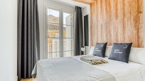 A modern bedroom with a bed, grey curtains, a wooden wall, and a balcony view. - Limehome Haro Calle de la Vega (Haro)