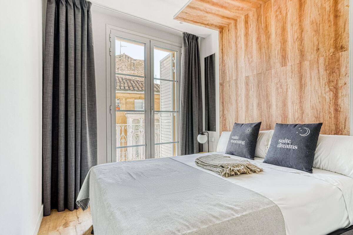 A modern bedroom with a bed, grey curtains, a wooden wall, and a balcony view.