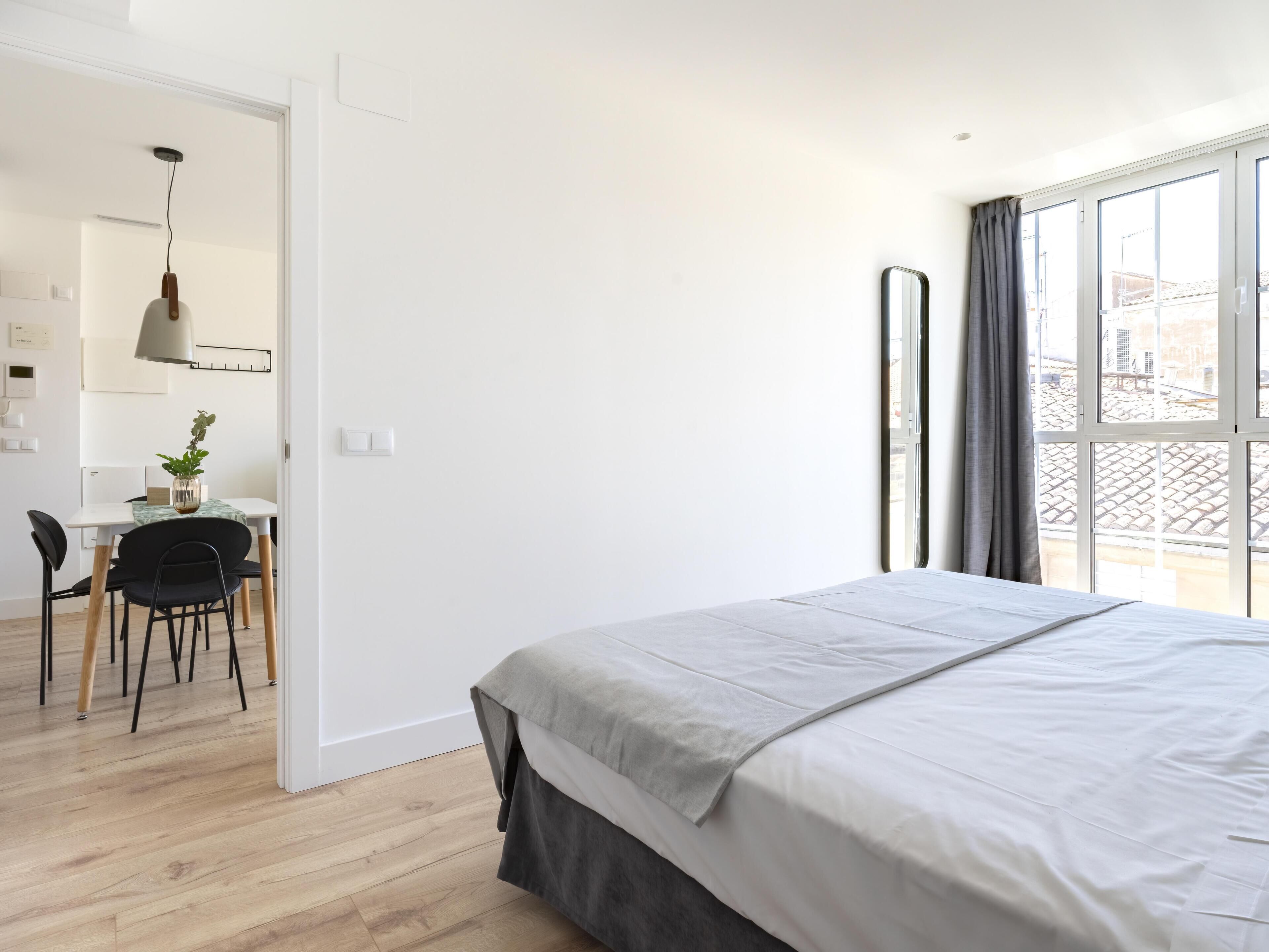 A bedroom with a large bed, a desk with a chair, and a view through a window.