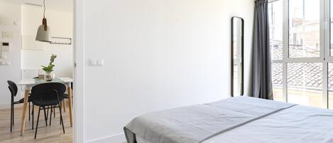 A bedroom with a large bed, a desk with a chair, and a view through a window.
