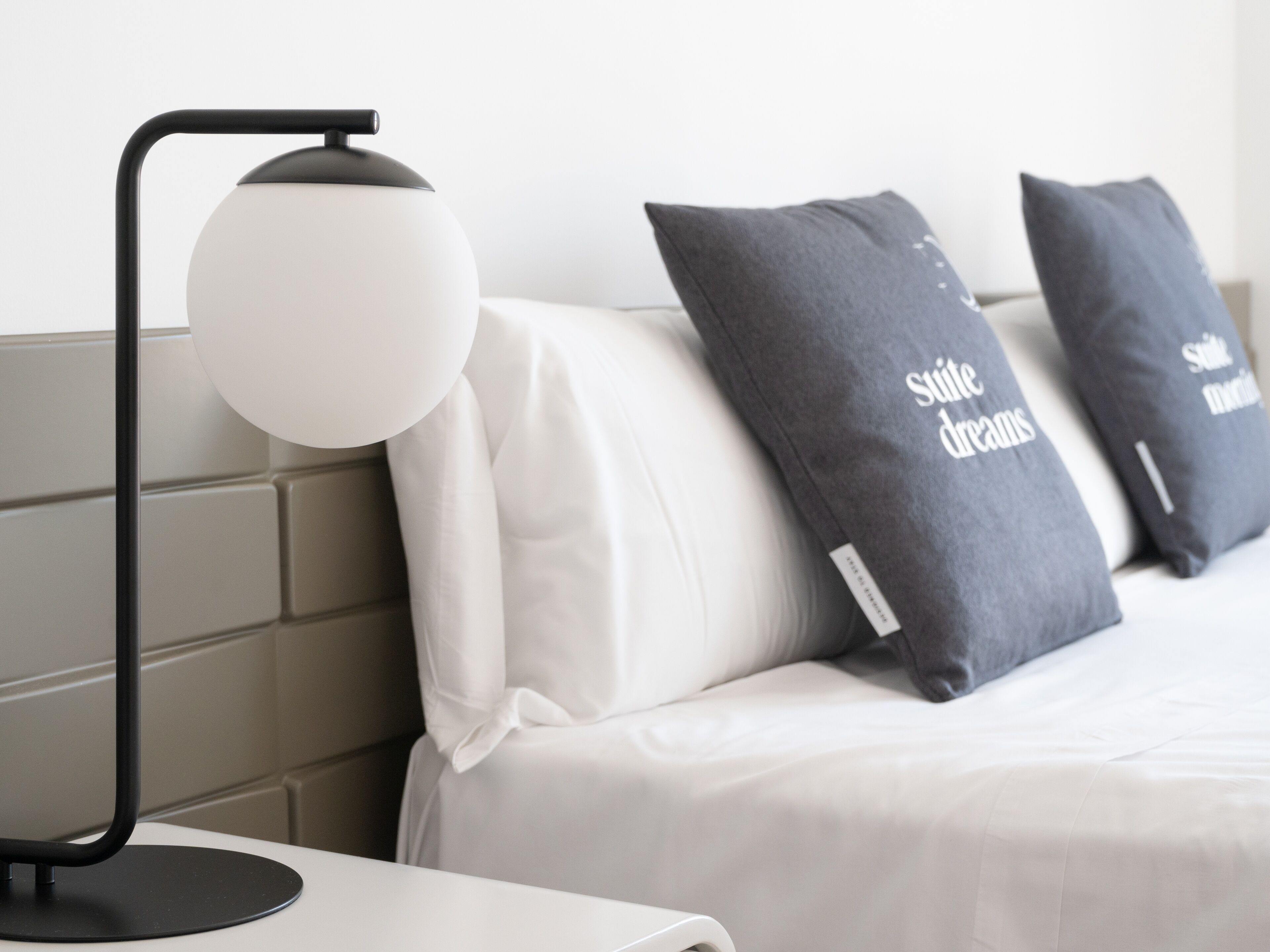 Un dormitorio moderno con cama, almohadas, mesita de noche y lámpara.
