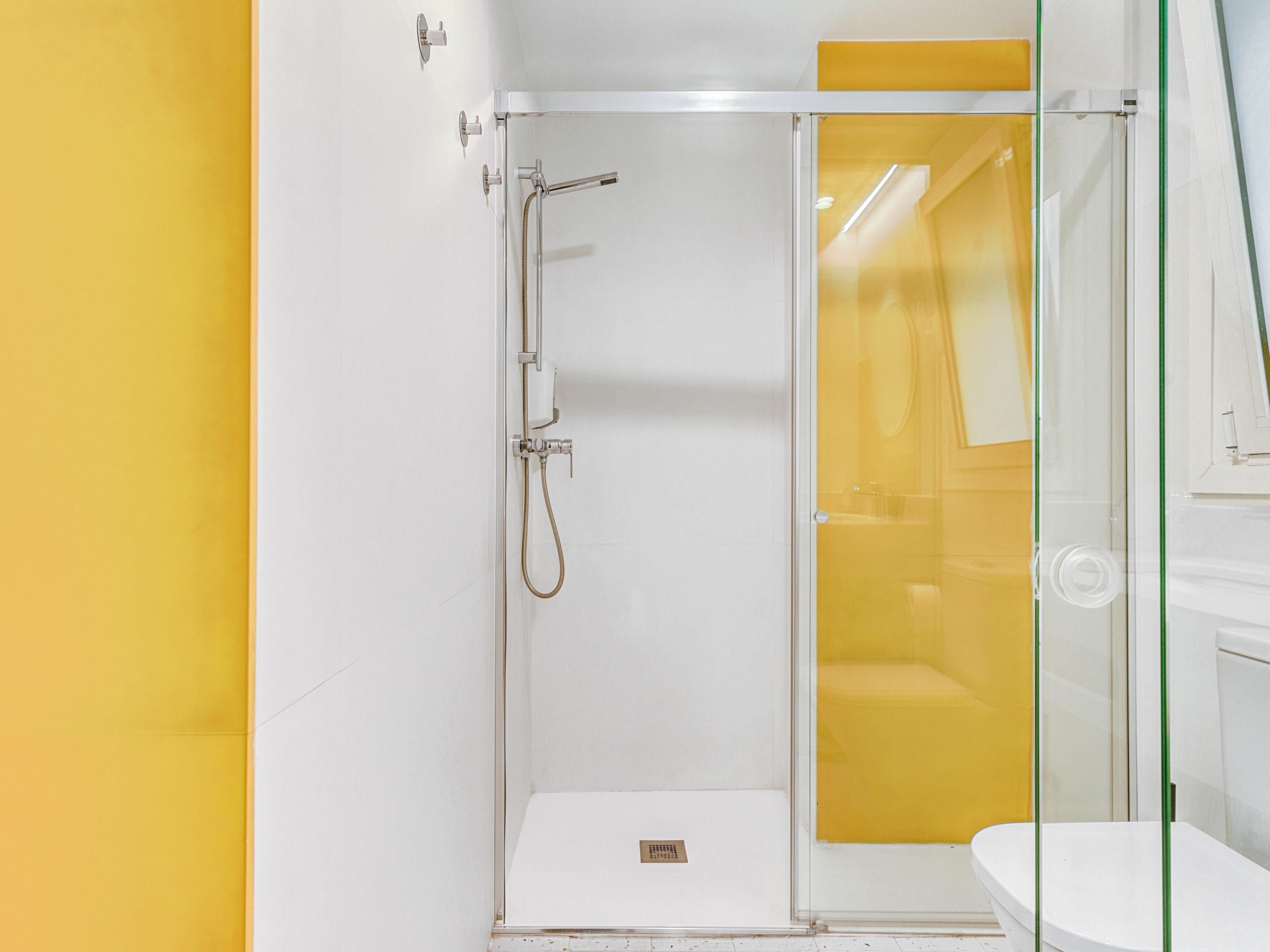 Une salle de bain moderne avec une douche à parois de verre, un lavabo blanc et un mur d’accent jaune.