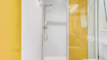 Une salle de bain moderne avec une douche à parois de verre, un lavabo blanc et un mur d’accent jaune.