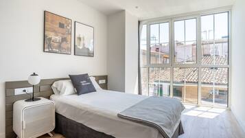 Un dormitorio con una cama, una mesita de noche, una ventana y dos cuadros colgados en la pared.