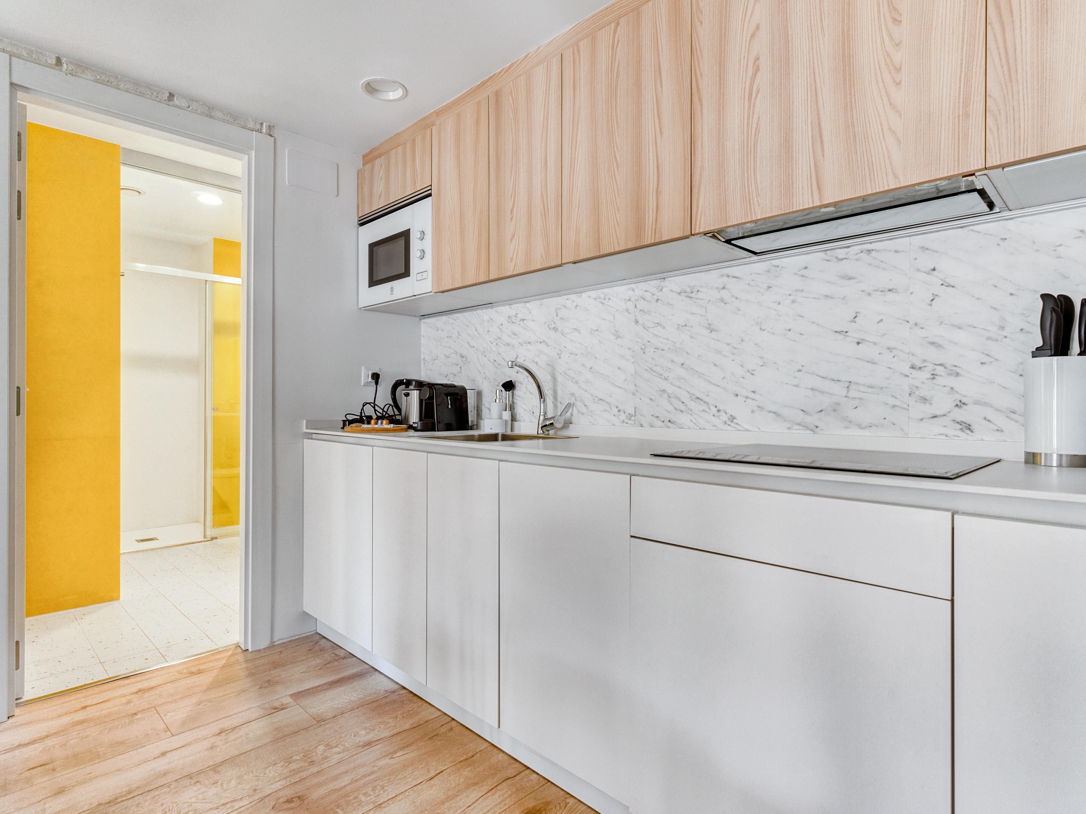 A modern kitchen with white cabinets, a marble backsplash, and a wooden door.