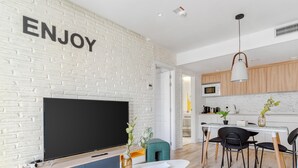 A modern living room with a large flat-screen TV, a dining area with a white table and chairs, and a kitchen with wooden cabinets and a white countertop. - Limehome Haro Calle de la Vega (Haro)
