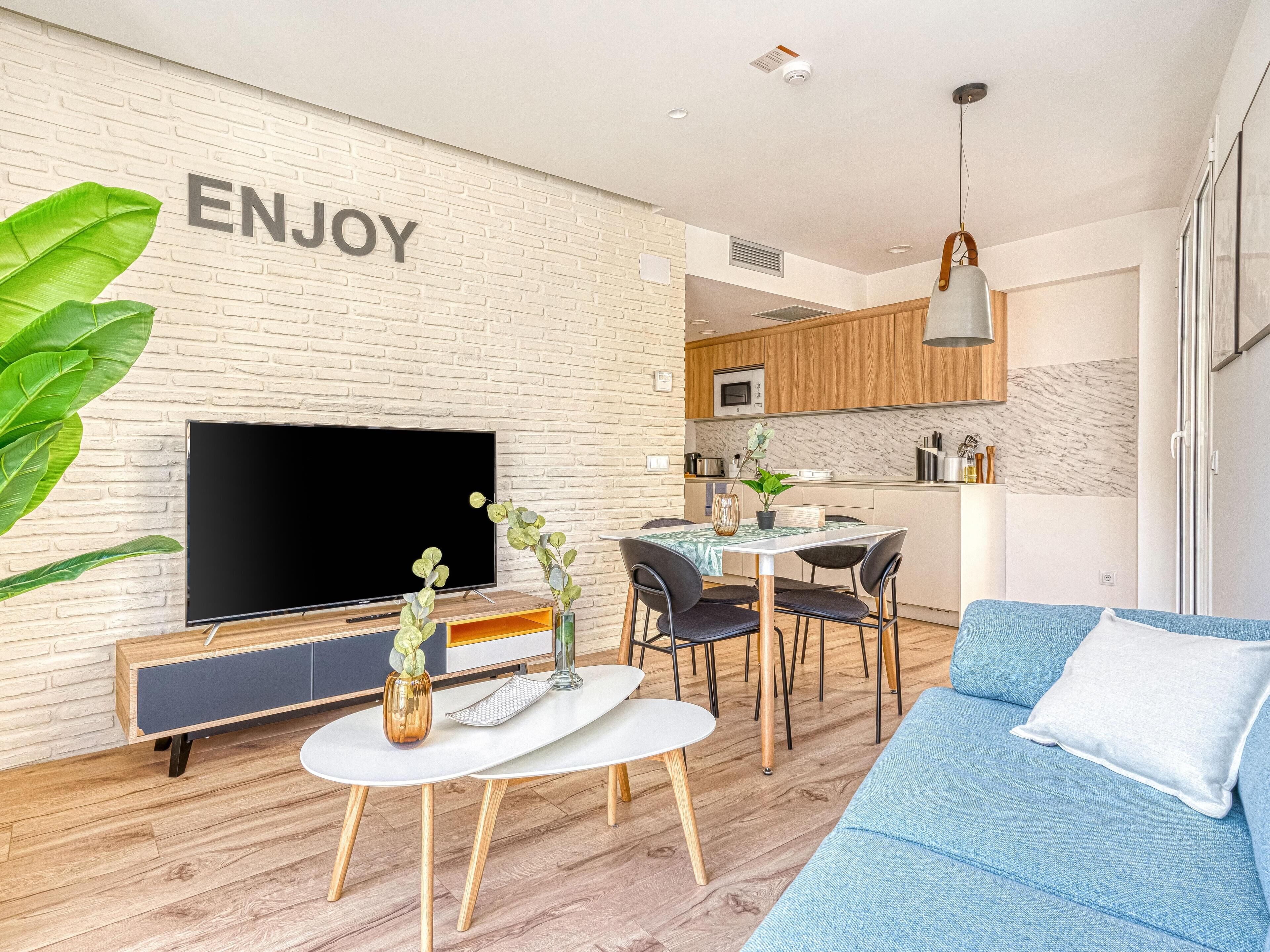 A modern living room with a flat-screen TV, a dining area, and a kitchen.