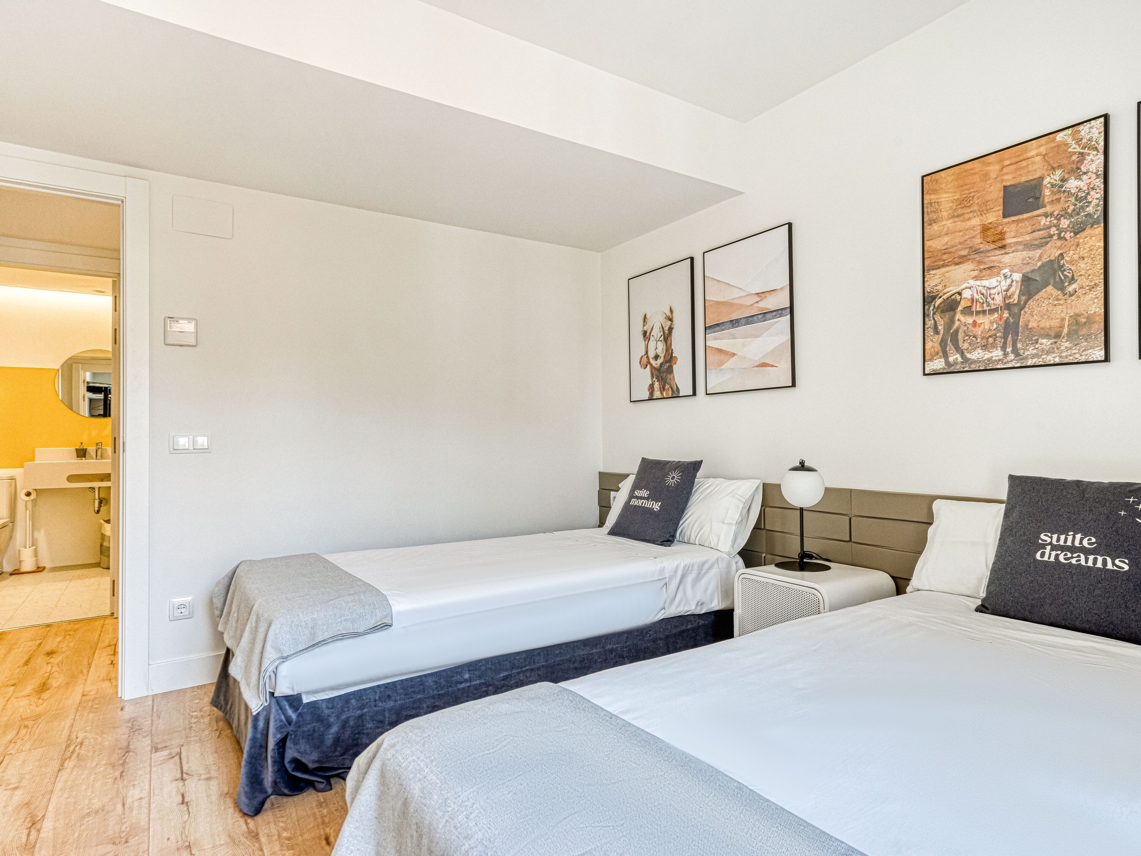 A hotel room with two beds, a bathroom, and a hallway.