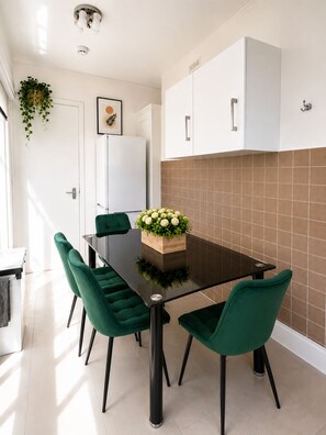 Une cuisine moderne avec des meubles blancs, un plan de travail noir et des chaises vertes.