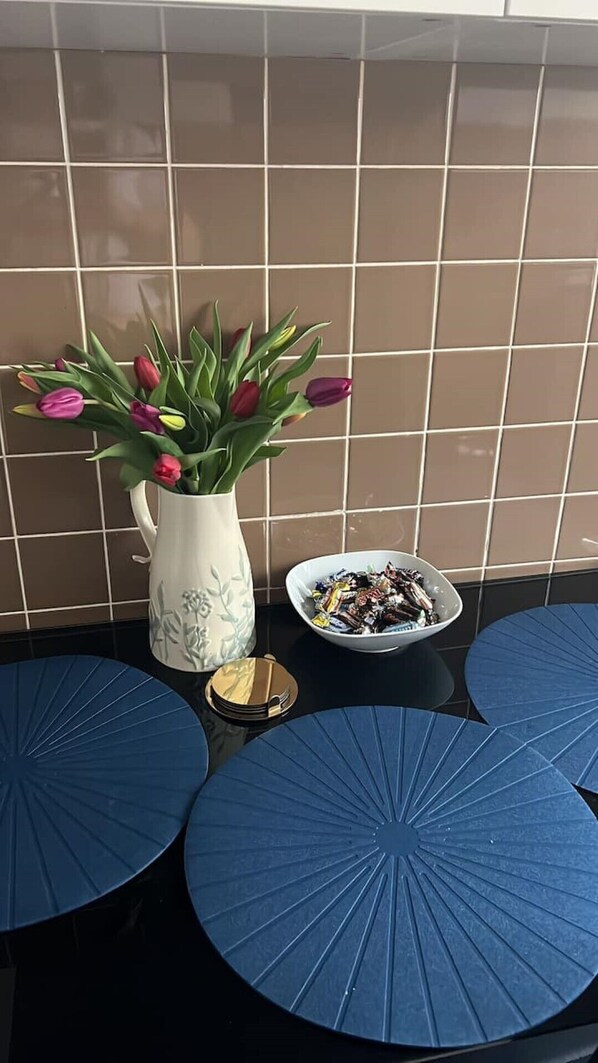 Un mur recouvert de carreaux, un vase blanc rempli de tulipes, un bol de chocolats et des tables rondes bleues.