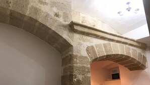 Una habitación con un arco de piedra que da a una ventana pequeña, una silla blanca y una mesa.