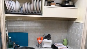 Cocina compacta con un lavamanos, escurreplatos y una encimera con diversos utensilios de cocina.
