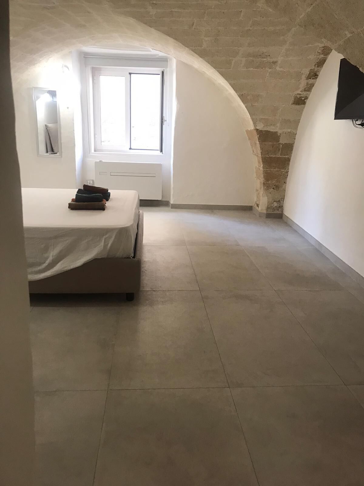 Un dormitori amb llit, finestra i paret de pedra.