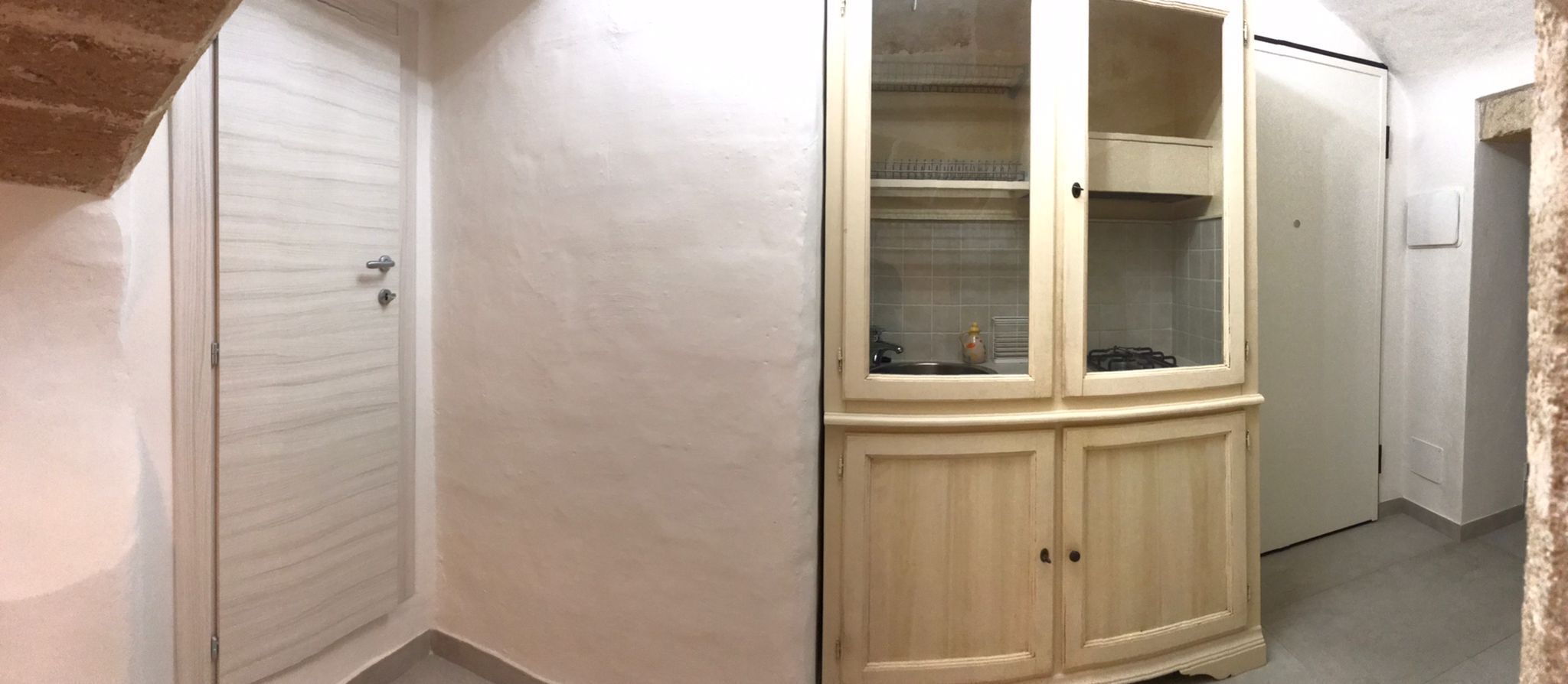 Un pasillo con un armario color crema con puertas de vidrio, una puerta blanca y un refrigerador blanco.