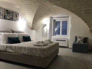 Une chambre avec un grand lit, un petit coin salon, une fenêtre donnant sur un beau paysage et des œuvres d’art accrochées au mur.
