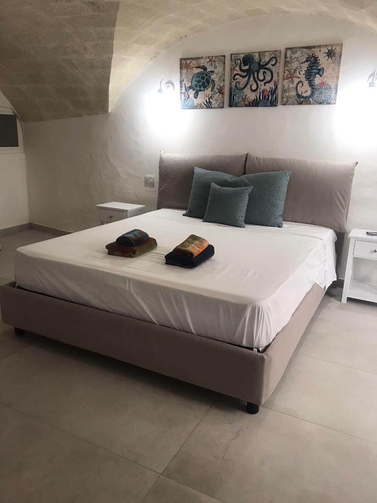 Une chambre à coucher avec un grand lit, deux oreillers, une table de chevet et un mur orné de trois œuvres d’art.