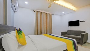 A hotel room with a bed, a grey armchair, a flat-screen TV mounted on the wall, and a ceiling fan. - Itsy Hotels Purple Suites (Bengaluru)