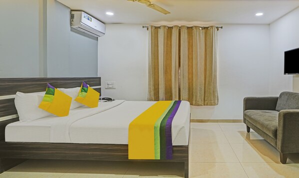 A hotel room with a bed, a sofa, a TV mounted on the wall, and a window with curtains. - Itsy Hotels Purple Suites (Bengaluru)