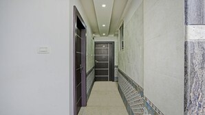 A narrow hallway with a dark door at the end, tiled walls, and a light switch on the left wall. - Itsy Hotels Purple Suites (Bengaluru)