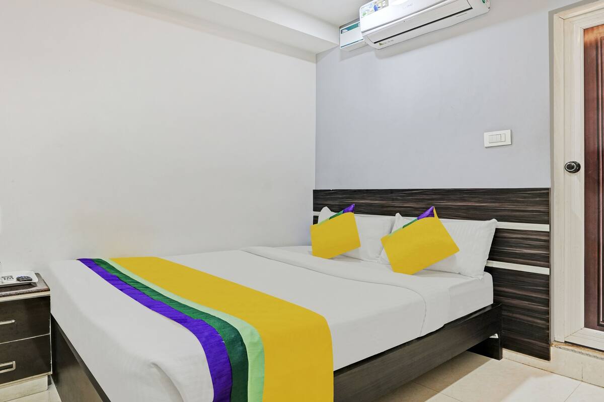 A neatly made bed with a white and multicolored bedspread, a wooden headboard, and a door with a geometric pattern.