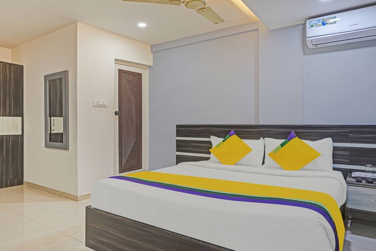 A hotel room with a bed, a wardrobe, a door, and an air conditioning unit.