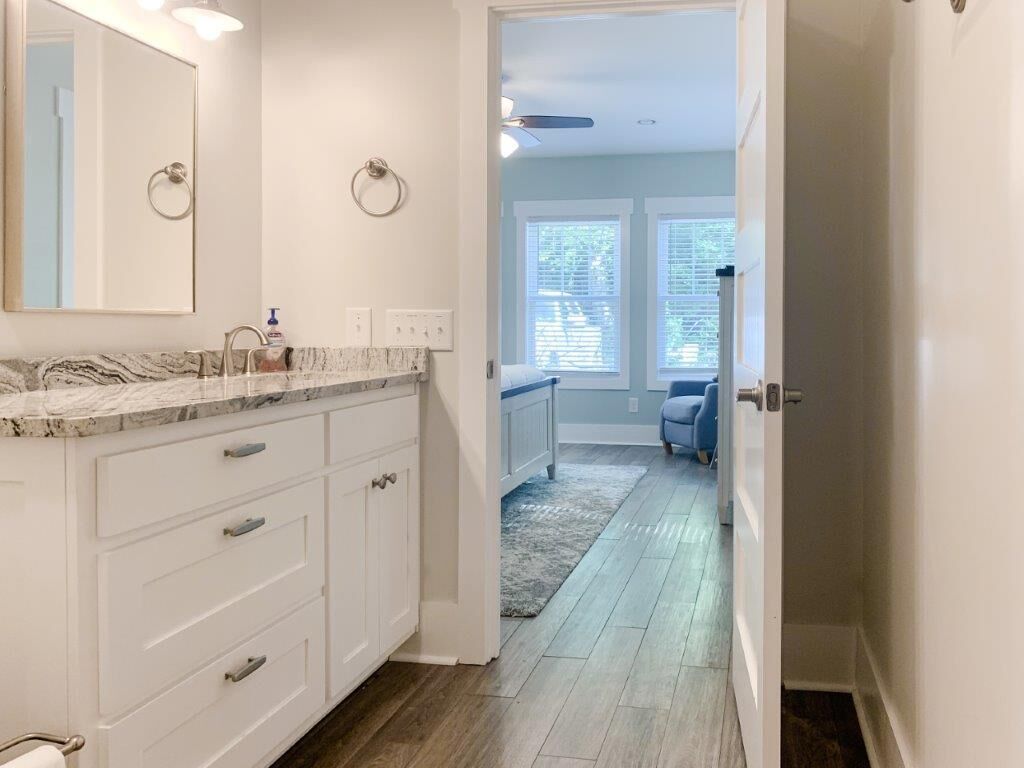 A bathroom with a marble countertop, white cabinetry, and a large mirror.