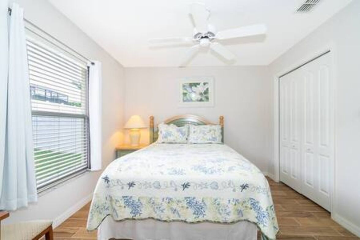 A bedroom with a bed, a ceiling fan, a window with blinds, and a door.