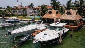 Uma marina com vários barcos atracados, uma construção com telhado de palha e um edifício com varandas.