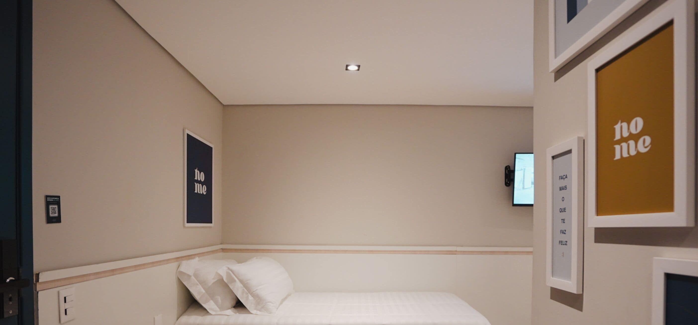 A hotel room with a bed, a wall-mounted TV, and two framed motivational posters.