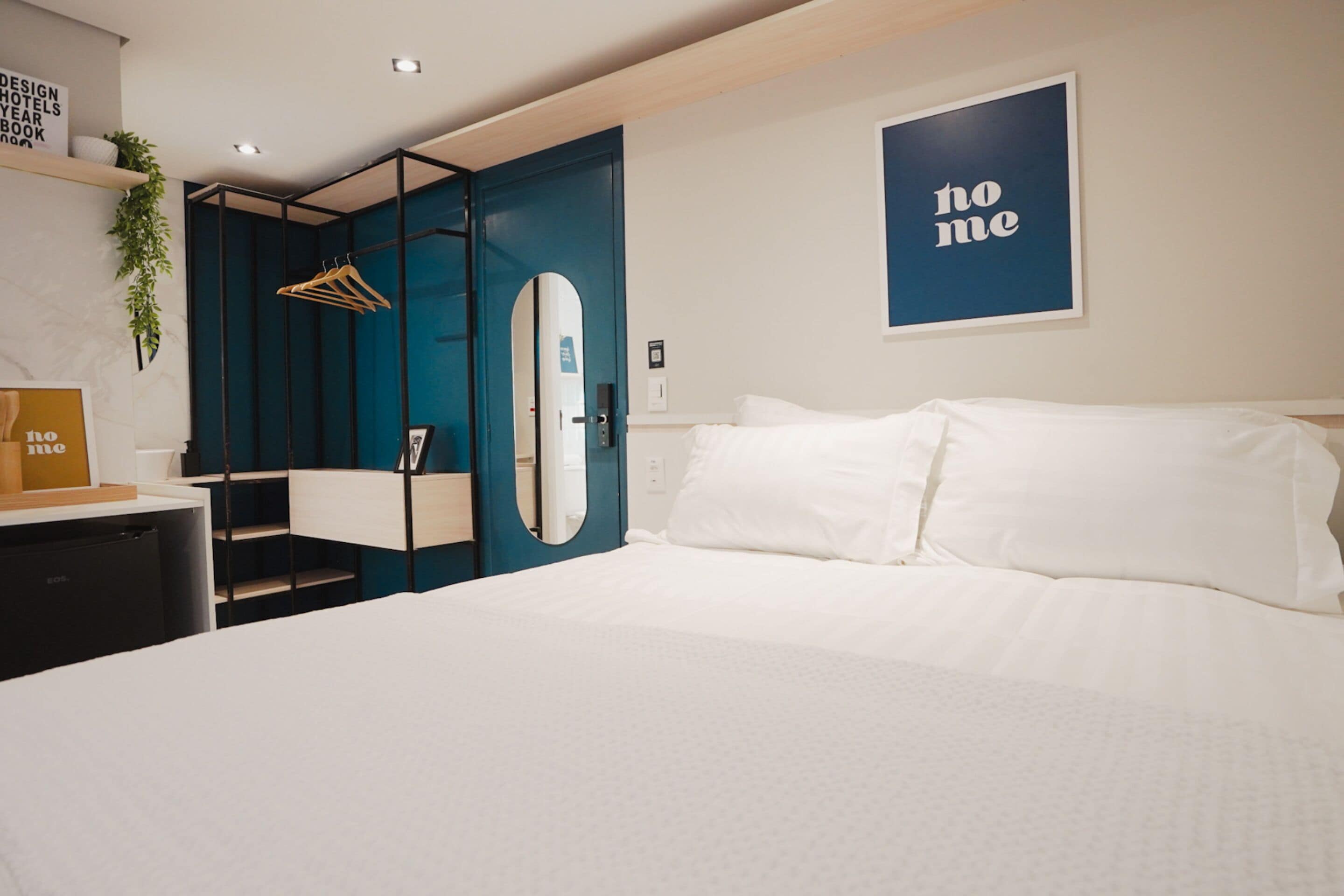 A modern hotel room with a large bed, a wardrobe with a mirror, and a 'home' sign on the wall.