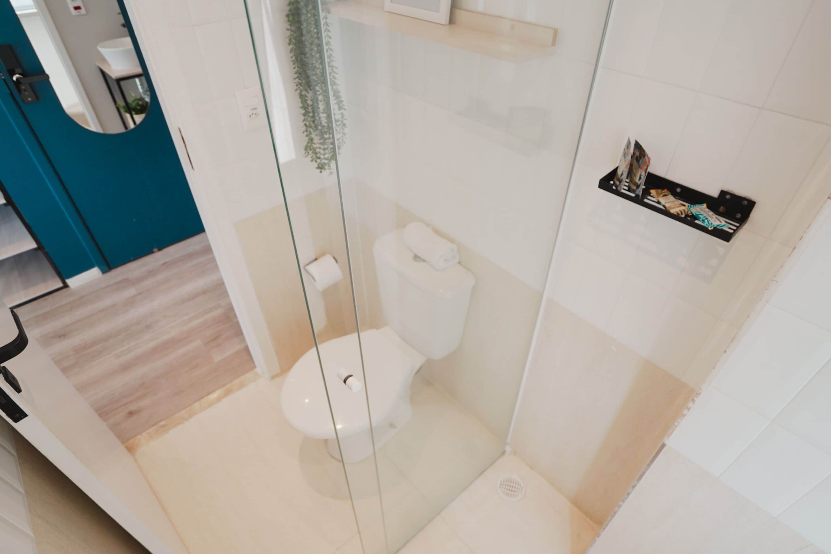 Ein modernes Badezimmer mit einer gläsernen Duschkabine, einer Toilette und einem Ablagefach mit Pflegeprodukten.